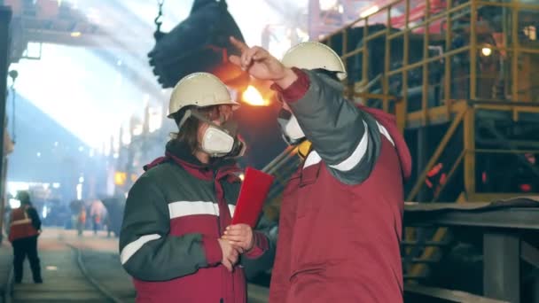 Muž a žena v respirátorech mluví v ocelárně. — Stock video