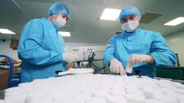 Tovární dělníci dávají na dopravník vany s pilulkami — Stock video