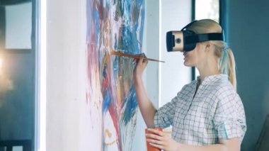 Sarışın kadın resim yaparken VR gözlük ve fırça kullanıyor.