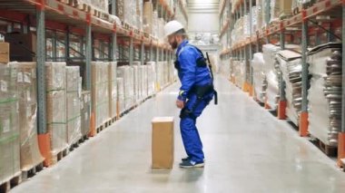 Depo işçisi ergoskeleton giyerken bir kutu kaldırıyor.