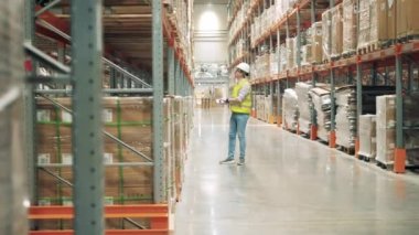Dizüstü bilgisayarı olan bir depo çalışanı paketlerle rafları inceliyor.