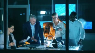 Uluslararası bilim adamları modern bir laboratuvarda bir robot kolu gözlemliyor..