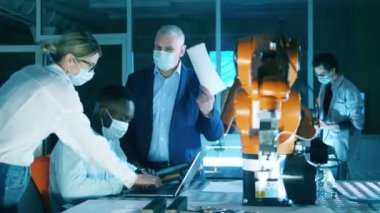 Yüz maskeli araştırmacılar robot laboratuarında konuşuyorlar.