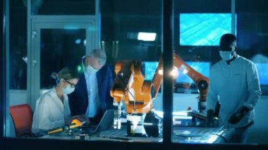 Yüz maskeli bilim adamları laboratuvarda robotları inceliyor.