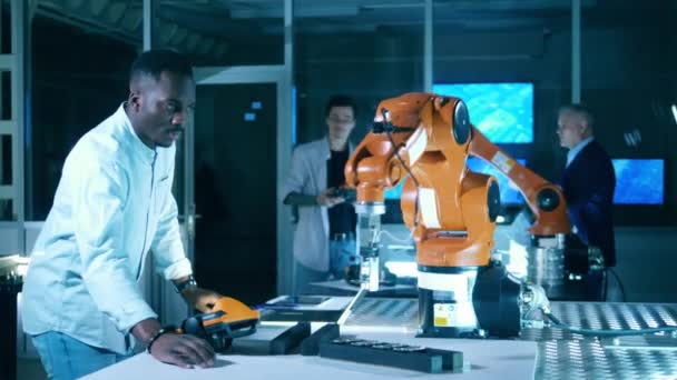 Afrikansk etnicitet forskare driver en robot med en elektronisk anordning. — Stockvideo