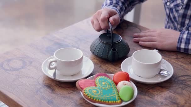 Een man giet thee. Vintage tafel, collorful cookies. — Stockvideo