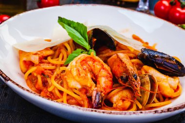 Beyaz tabakta deniz ürünleri, domates ve parmesan peynirli makarna.