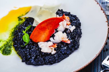 Beyaz tabakta ıstakoz ve parmesan peynirli siyah mürekkep balığı pilavı..