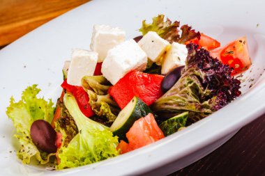 Taze sebzeli Yunan salatası, beyaz tabakta beyaz peynir ve siyah zeytin.