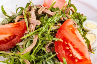 Beyaz tabakta roka, domates ve bıldırcın yumurtası ile sığır dili salatası.