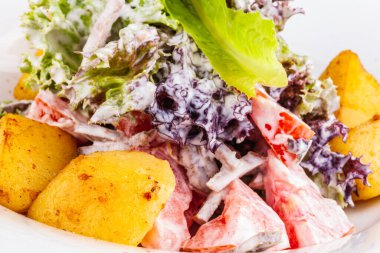 Beyaz tabakta fırında patates, domates, marul ve sığır dili ile salata.