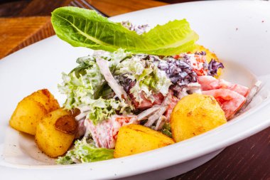 Beyaz tabakta fırında patates, domates, marul ve sığır dili ile salata.