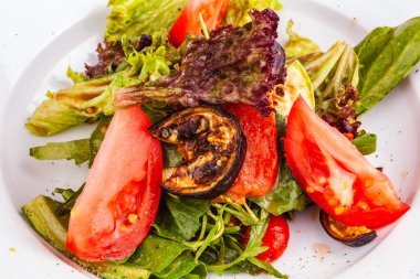 Taze ve ızgara sebzeli salata ve yeşil yapraklar beyaz tabakta karıştırılır. Sağlıklı vejetaryen yemekleri