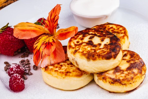 Kahvaltıda. Süzme peynirli krep, şurup taze böğürtlenli krep ve çilekli çilek, beyaz tabakta ekşi krema. Rus ya da Ukrayna mutfağı.