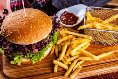 Bir sepet patates kızartmalı hamburger ve ahşap kesim tahtasına domates sosu.