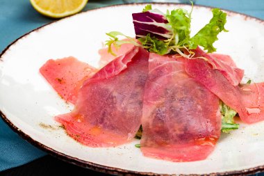 Beyaz tabakta taze yeşil salata ile ton balığı carpaccio.