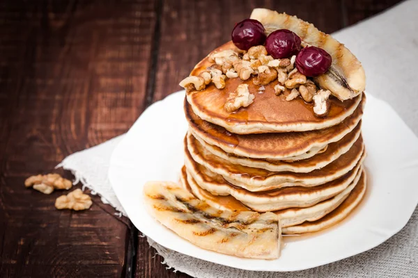 Pannkakor med körsbär, grillad banan och nötter på en mörk bakgrund — Stockfoto