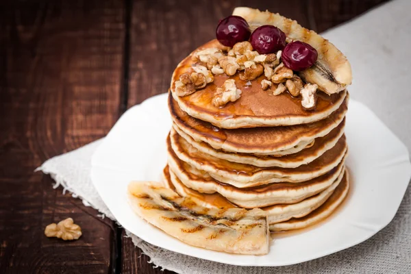 Pannkakor med körsbär, grillad banan och nötter på en mörk bakgrund — Stockfoto