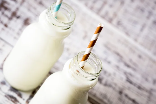 Two bottles of milk with striped straws standing on old table.