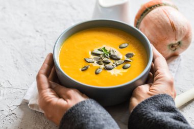 Kabak ve havuç kremalı çorba, kabak çekirdeği ve kızarmış ekmek. Kadın elleri bir tabak tutuyor.