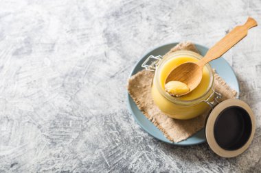 Kavanozda tereyağı ve gri masada tahta kaşık. Üst Manzara. Kopyalama. Ghee yağı sağlıklı yağlıdır ve Hint yemeklerinin çoğunda yaygın bir yemek malzemesidir.