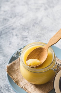 Kavanozda tereyağı ve gri masada tahta kaşık. Üst Manzara. Kopyalama. Ghee yağı sağlıklı yağlıdır ve Hint yemeklerinin çoğunda yaygın bir yemek malzemesidir.