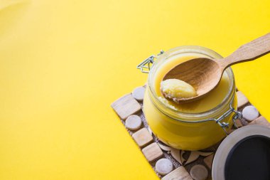 Kavanozda tereyağı ve sarı arka planda tahta kaşık. Üst Manzara. Kopyalama. Ghee yağı sağlıklı yağlıdır ve Hint yemeklerinin çoğunda yaygın bir yemek malzemesidir.