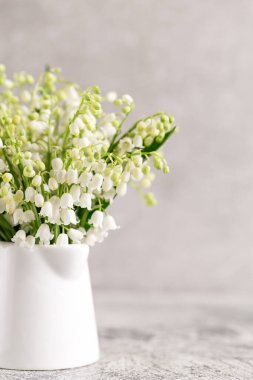 Beyaz bir bardakta, gri bir arka planda, vadideki zambaklar..