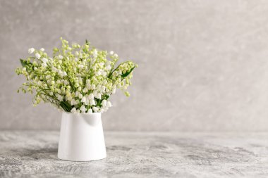 Beyaz bir bardakta, gri bir arka planda, vadideki zambaklar..