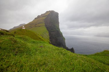 Faroe Adaları 'ndaki güzel dramatik manzara. Bulutlu gökyüzü, deniz feneri, çimen