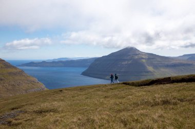 Faroe Adaları 'nda güzel genç bir çift yürüyor. Deniz, bulutlar, dağlar, güzel manzara.