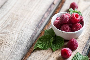 Tahta bir masada yeşil yapraklı taze ahududu..
