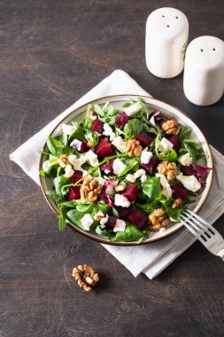 Taze roka ile pancar veya pancar salatası, tabakta yumuşak peynir ve ceviz, koyu ahşap arka planda sos ve baharatlar, fotokopi alanı, üst görünüm
