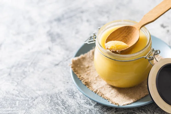 Kavanozda tereyağı ve gri masada tahta kaşık. Üst Manzara. Kopyalama. Ghee yağı sağlıklı yağlıdır ve Hint yemeklerinin çoğunda yaygın bir yemek malzemesidir.