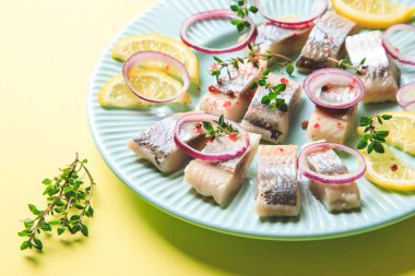 Baharatlı tuzlu ringa balığı, otlar ve soğan tabakta, sarı arka planda fotokopi alanı ile birlikte. Salamura edilmiş balık. Sağlıklı doymamış yağlı yiyecekler, Omega 3. Üst manzara, düz uzanma