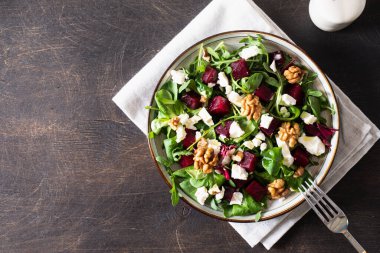Taze roka ile pancar veya pancar salatası, tabakta yumuşak peynir ve ceviz, koyu ahşap arka planda sos ve baharatlar, fotokopi alanı, üst görünüm