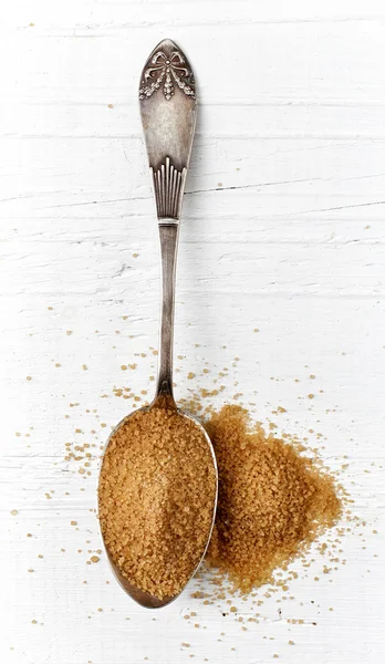 Brauner Zucker in metallischem Löffel auf weißem Holztisch — Stockfoto