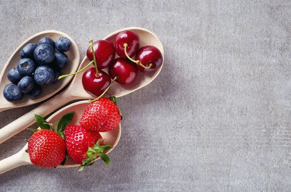 Bleuets, cerises et fraises dans des cuillères en bois, d'en haut — Photo