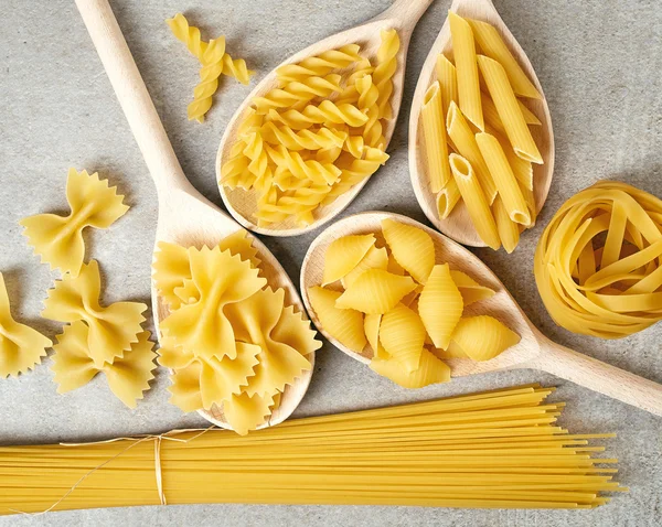 Varios tipos de pasta sobre fondo gris, desde arriba — Foto de Stock