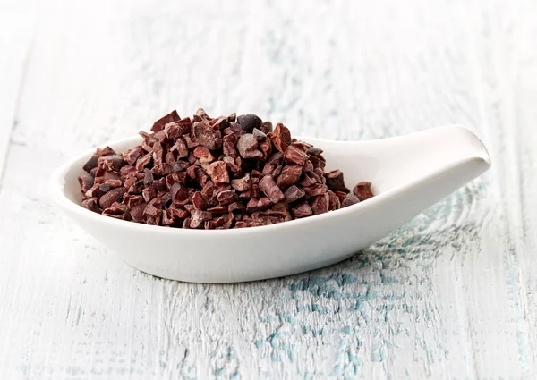 Cacao nibs in porcelain spoon — Stock Photo, Image