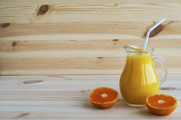 Orangensaft im Krug und Mandarinen auf einem Holztisch. — Stockfoto