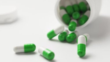 Beyaz-yeşil kapsüller şişeden masaya düşüyor, ağır çekimde. Antiviral ilaçlar, virüs koruması, Covid-19 tedavisi.