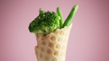Lezzetli brokolinin üzerine siyah beyaz susam düştü. Yeşil fasulye ve brokoli bir waffle bardağında pembe arka planda döner. Vegan gıda konsepti. Fast food yerine sağlıklı yemek..