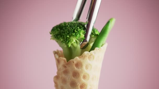 花椰菜用钳子放在华夫饼杯中 青豆和西兰花在华夫饼杯中旋转着粉红的背景 食物的概念 以健康食品取代快餐 — 图库视频影像