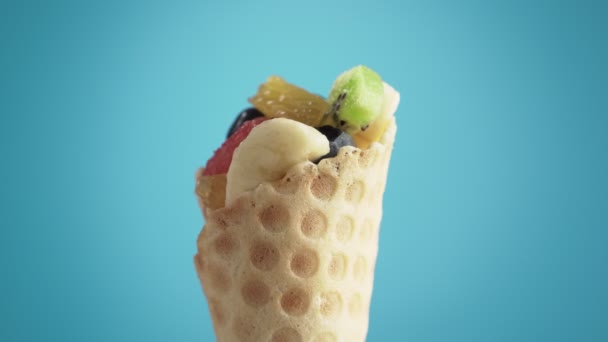ワッフルコーンにブルーベリーを入れたフレッシュでジューシーなフルーツサラダが青色の背景で回転します ビーガンフードコンセプト — ストック動画
