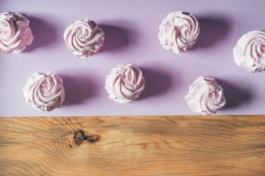 Ahşap ve mor arka planda taze marşmelovlar. Zephyr, kremalı pasta. Ev yemeği konsepti, tatlılar. Minimalizm, üst görünüm, düz görünüm, telif alanı.
