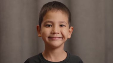 Basit bir arka planın önünde duran parlak bir gülümsemeyle ışıldayan genç bir çocuğun portresi. Siyah tişörtlü, koyu renk saçlı, gülümseyen neşeli çocuğa yakın durun..