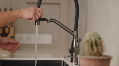 Bilinmeyen kişi, parlak mutfakta lavaboyu parlak modern muslukla ustalıkla yıkıyor. Tanınmayan adam, modaya uygun musluğun esnek hortumunun işlevlerini gösteriyor.