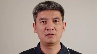 Confused asian man scratching his head with puzzled and uncertain facial expression in neutral studio environment. His face expresses misunderstanding, doubt, problem awareness, hesitation.