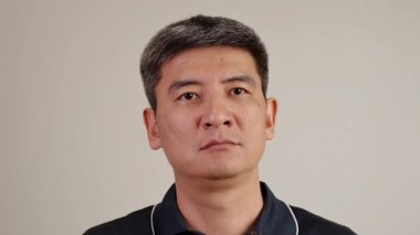 Pensive middle-aged person with straight face touching his chin while looking upward in deep consideration, captured against a clean neutral studio background.